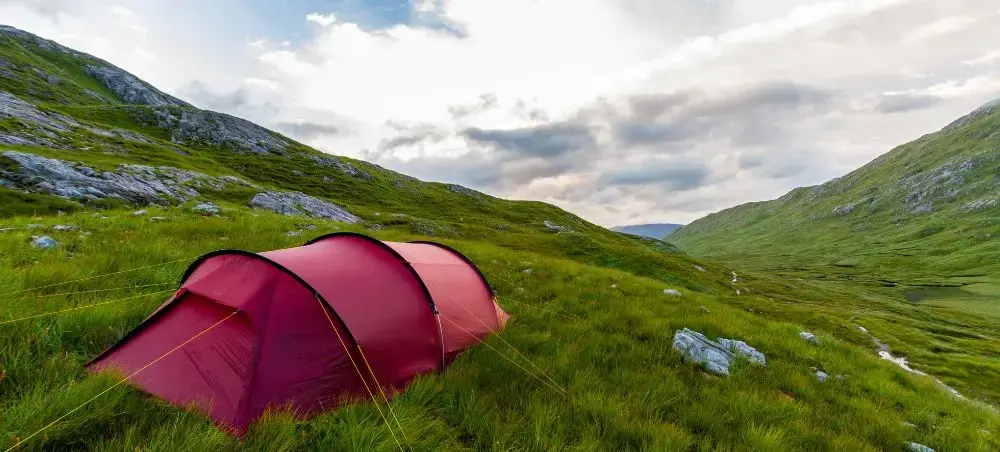 Red camping tent pitched on grassland in a Scottish glen, illustrating remote destinations accessible via private jet charter