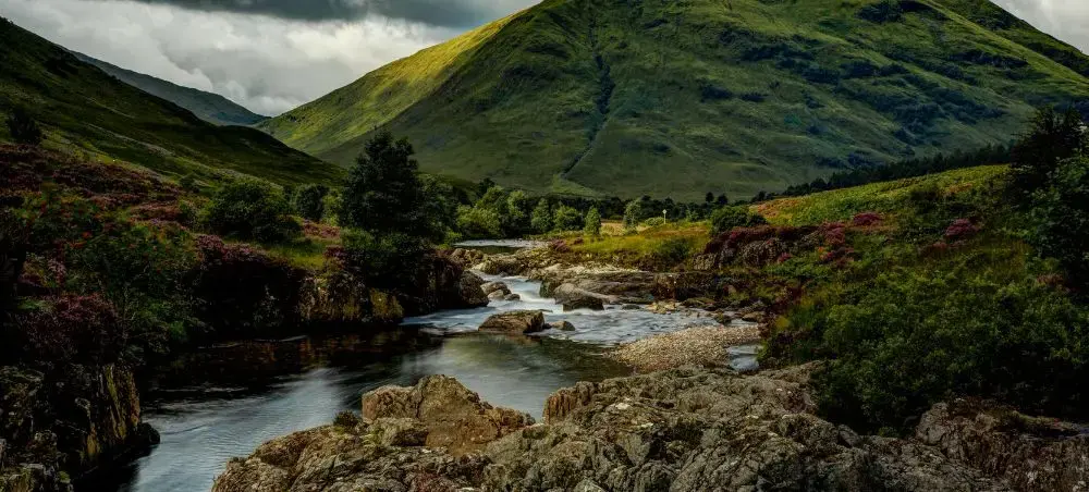 Rocky river winding through the Scottish Highlands with lush green mountains and heather-covered slopes