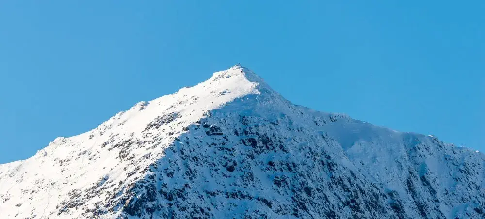 Snow-capped summit of Snowdon in Eryri National Park under a clear blue winter sky, a private jet destination in North Wales
