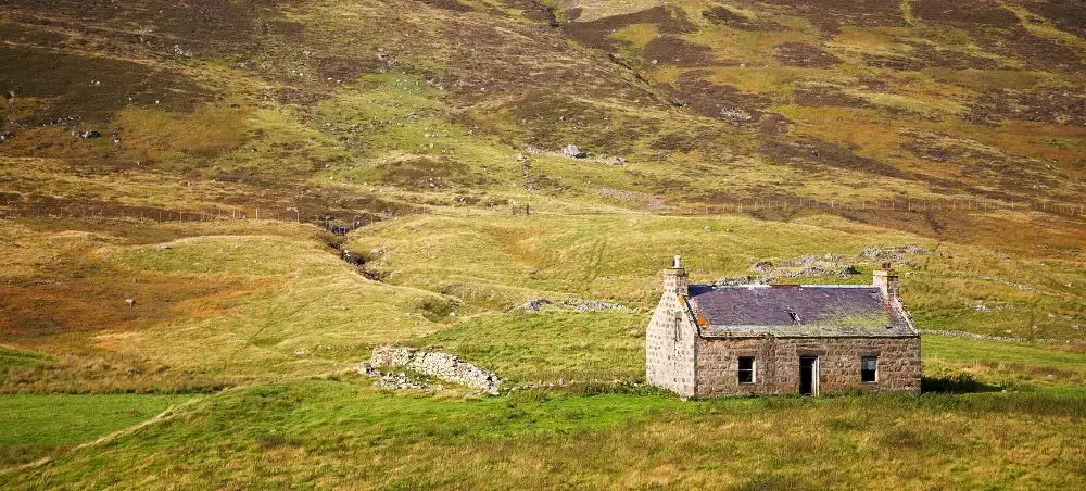 Abandoned stone crofthouse nestled in the rolling moorland hills of Speyside, Scotland, evoking the remote Highland landscape