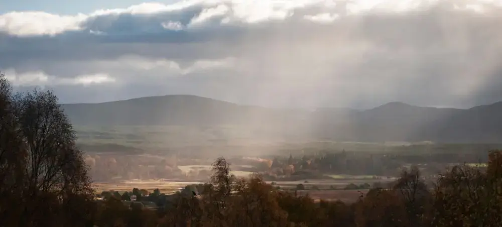 Panoramic autumn view over the Speyside valley in Scotland, with rolling hills, misty light rays, and golden woodland