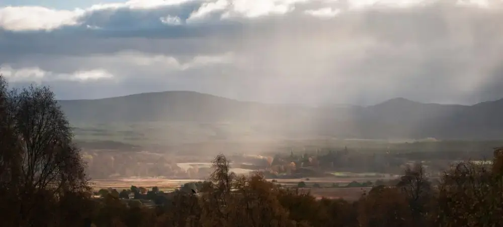 Dramatic Scottish Highlands valley with autumn foliage, rolling hills, and misty sunlight breaking through clouds in Speyside, Scotland