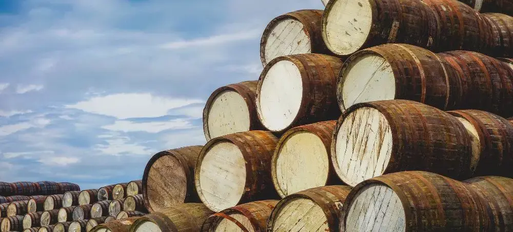 Rows of aged oak whisky barrels stacked outdoors at a Speyside distillery under a cloudy Scottish sky