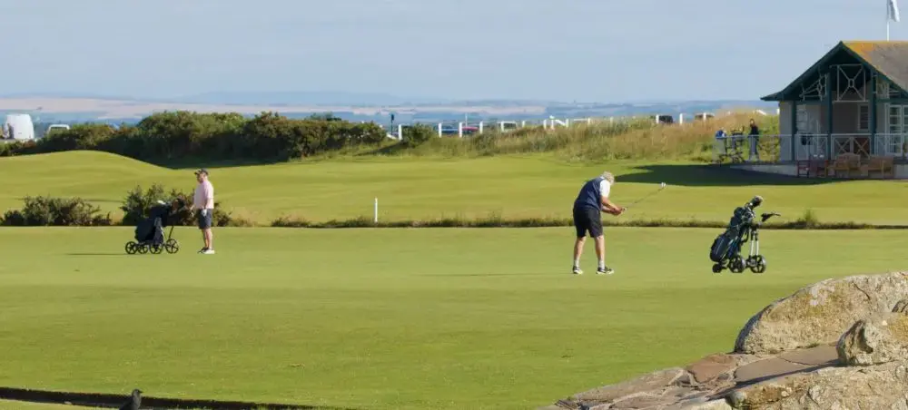 Golfers playing on the iconic links fairway at St Andrews golf course, with the historic clubhouse and coastal landscape