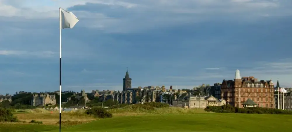 Golf green with white flag at St Andrews Links, with the historic St Andrews town skyline and grand hotel in the background