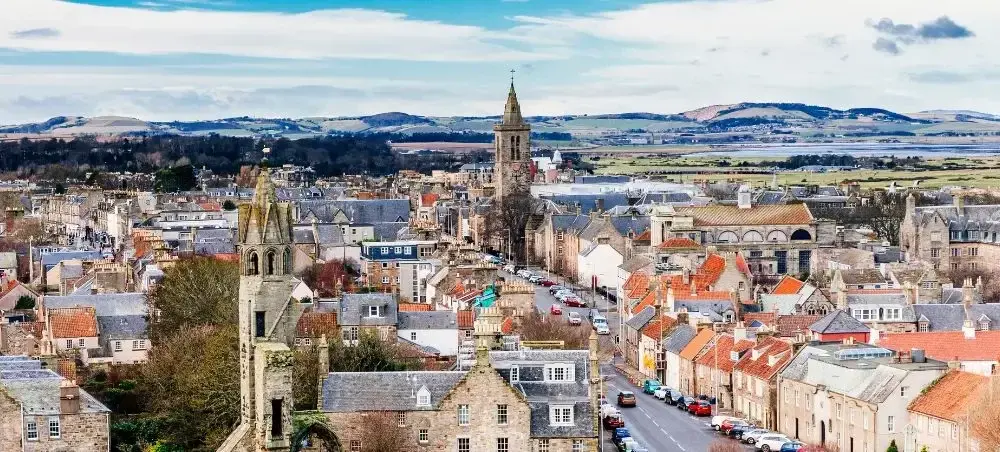 Aerial panoramic view of St Andrews, Scotland, showcasing historic stone buildings, church spires, and rooftops
