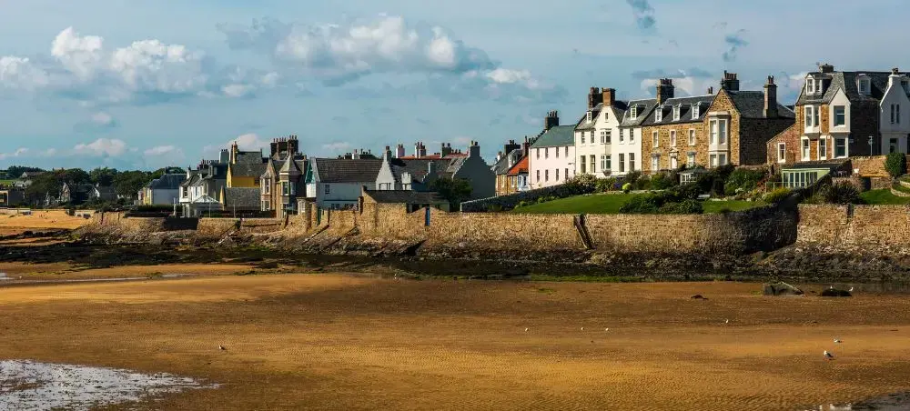 Golden sandy beach at low tide in St Andrews, Scotland, with a row of traditional stone townhouses and whitewashed villas