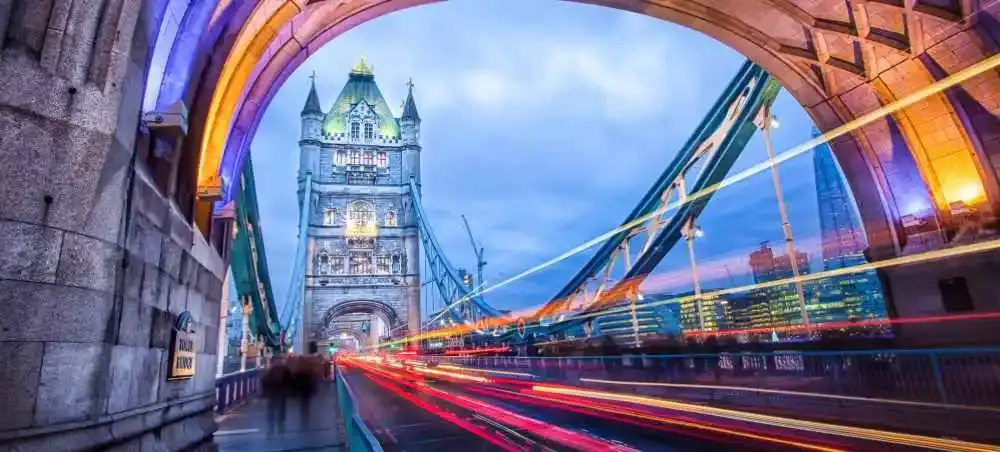 Tower Bridge illuminated at dusk with light trails from traffic streaming through its iconic Gothic arch, London, England