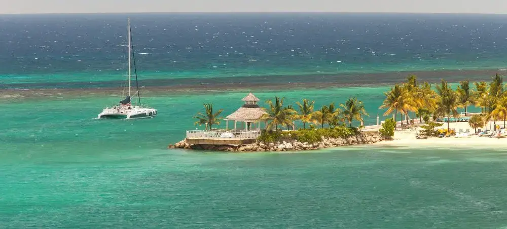 Tropical island of Ocho Rios, Jamaica with a yacht sailing in the background