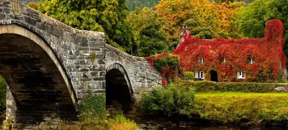 Stone arch bridge beside a Welsh cottage during autumn, a scenic UK countryside destination accessible by private jet charter