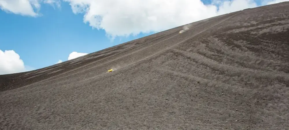 Thrill-seekers volcano boarding down the steep dark ash slopes of Cerro Negro volcano near León, Nicaragua