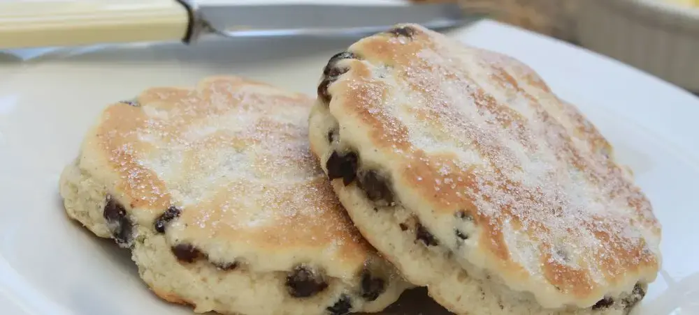 Freshly baked Welsh cakes dusted with sugar on a white plate, a traditional treat to enjoy when visiting Bannau Brycheiniog