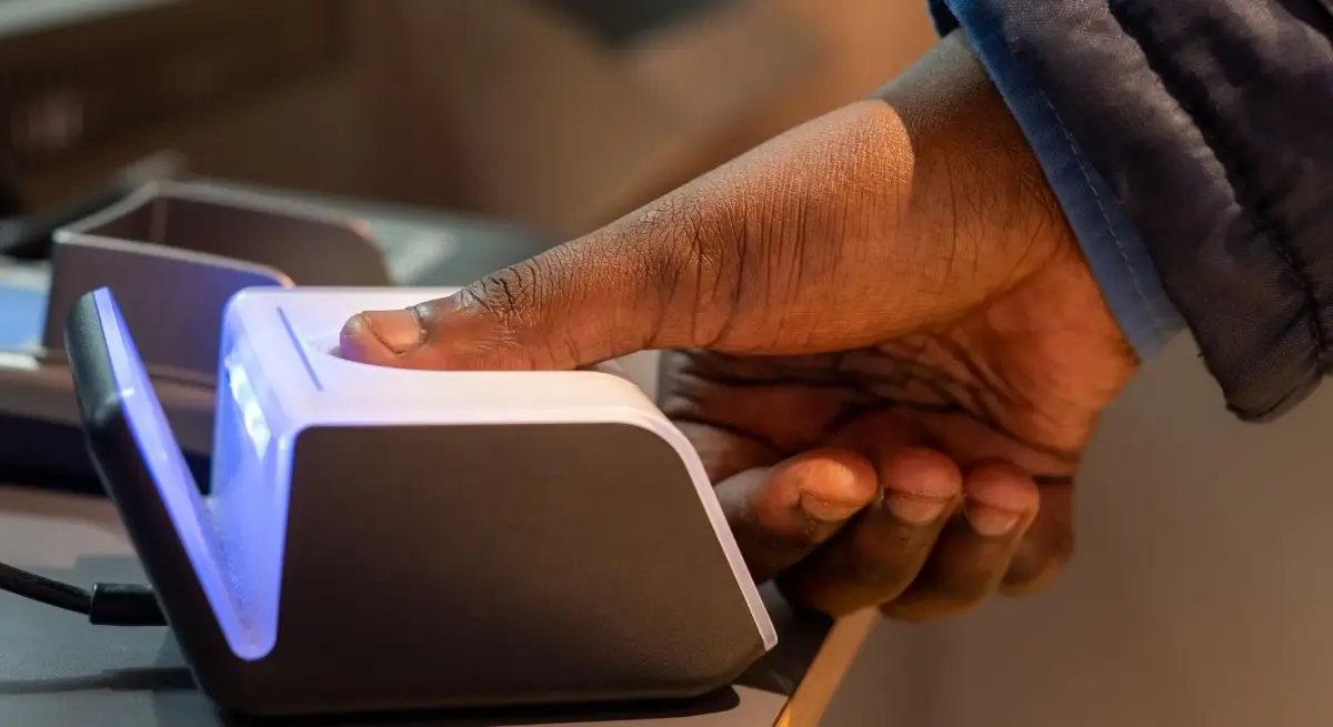 Traveller pressing thumb onto a blue-lit biometric fingerprint scanner during private jet border security screening in 2025