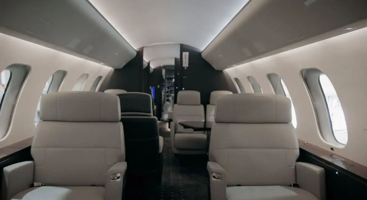 Spacious Bombardier private jet cabin interior with cream leather seats, ambient overhead lighting, and oval windows along both sides