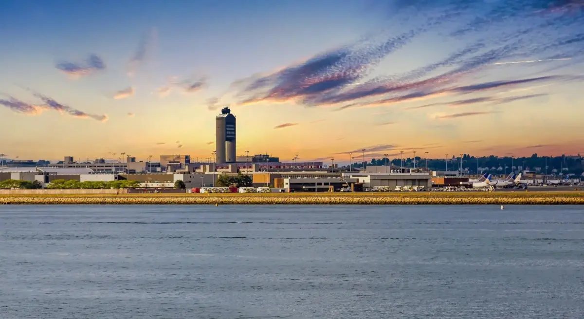 Boston Logan International Airport viewed across the waterfront at sunset, with air traffic control tower and aircraft