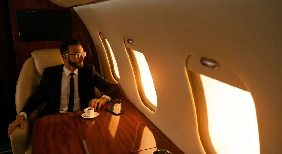 Business executive in a suit seated in a luxury private jet cabin with espresso and smartphone, gazing out oval windows over Singapore