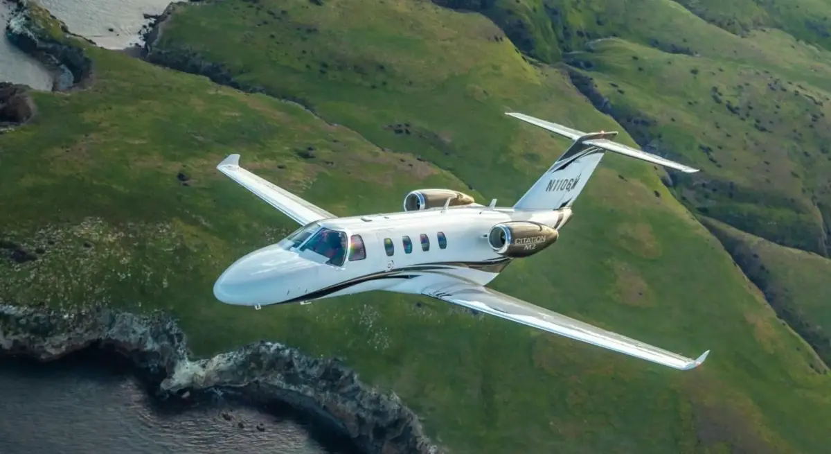 Cessna Citation M2 light private jet cruising over lush green coastal cliffs, representing modern charter aviation in 2025