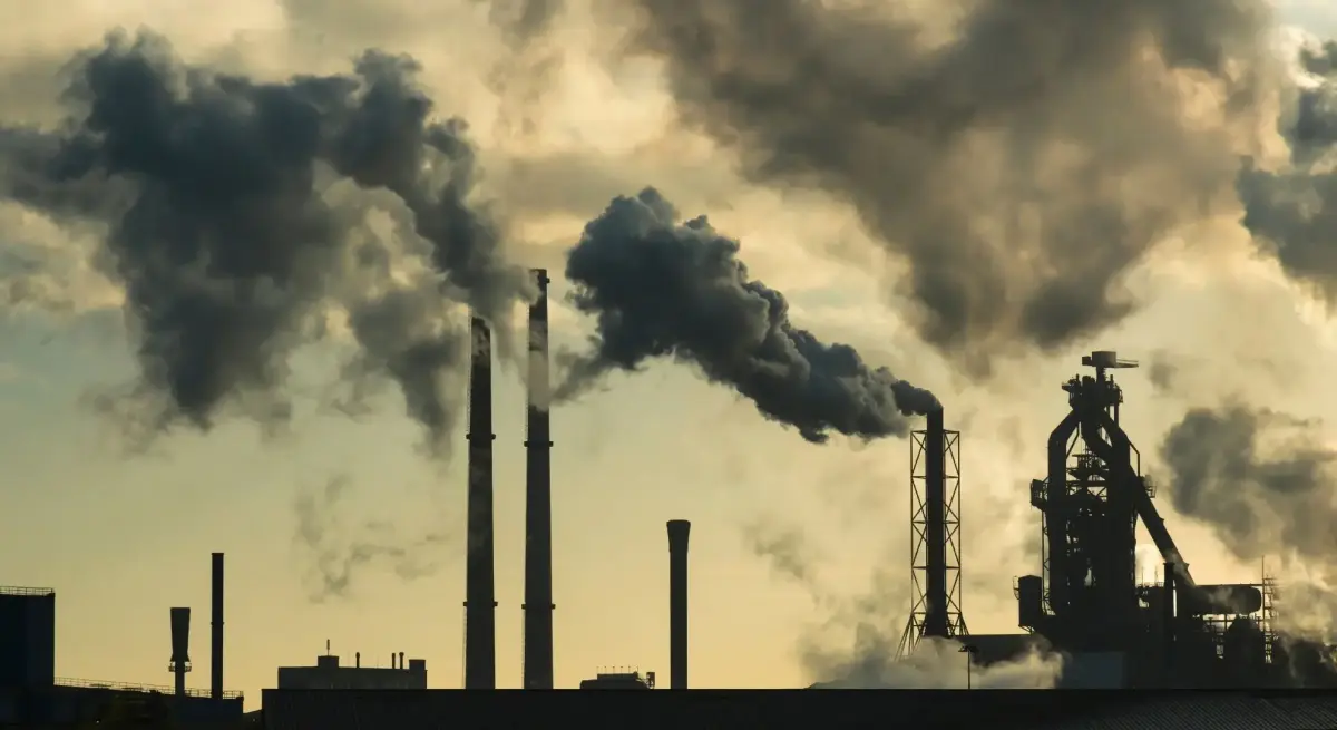 Industrial smokestacks billowing heavy dark emissions against a hazy sky