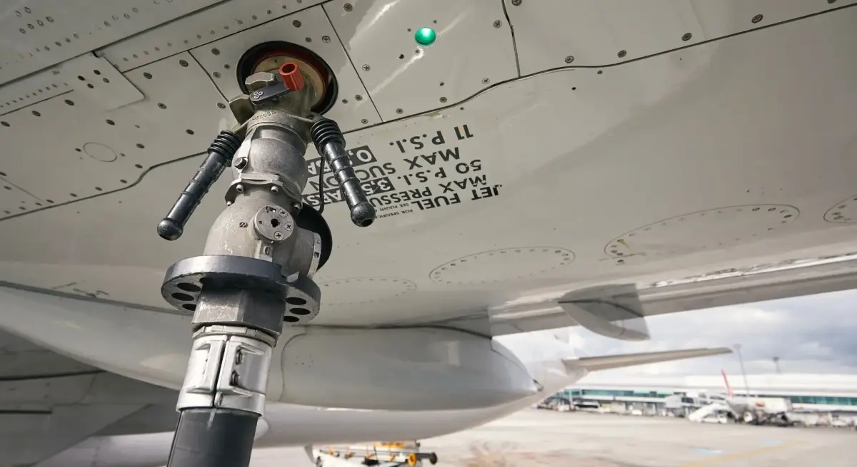 Jet fuel nozzle connected to an aircraft wing underside fuel port, with max pressure specifications visible, on an airport apron