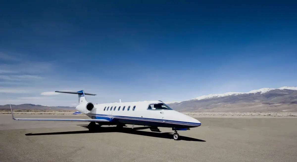 Learjet light jet parked on a desert tarmac with snow-capped mountains