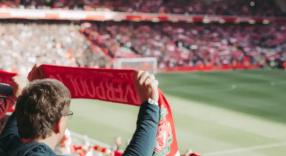 Liverpool FC fan holding a red club scarf aloft inside a packed Anfield stadium