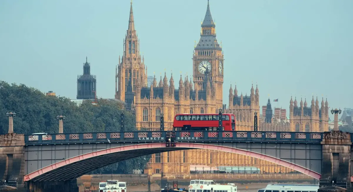 Red double-decker bus crossing Lambeth Bridge with the Houses of Parliament and Big Ben towering behind