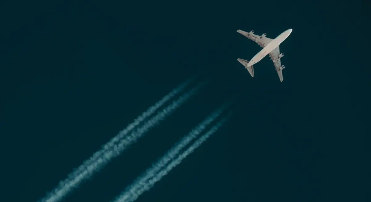 Large jet aircraft cruising at high altitude against a deep blue sky, leaving twin contrails as it speeds across the atmosphere