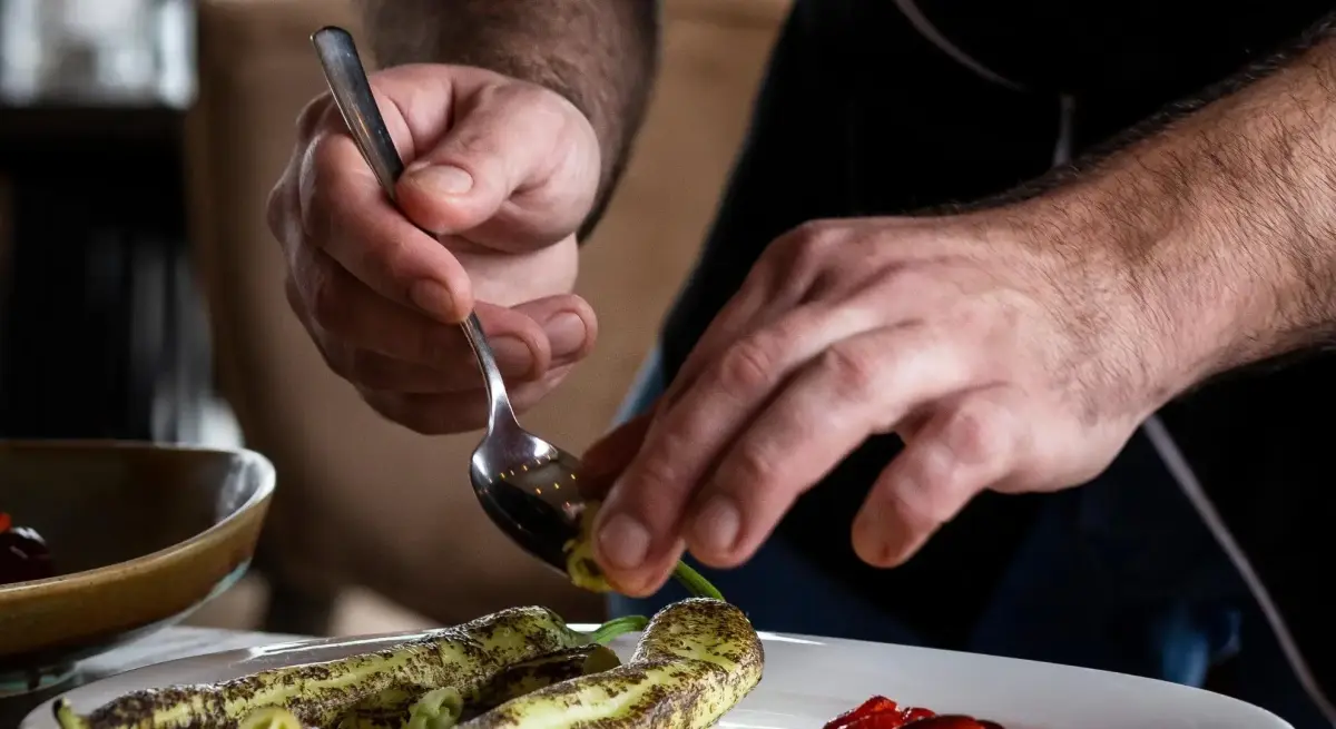 Chef meticulously plating a gourmet dish with herb-dusted vegetables and sauce on a private charter flight culinary service