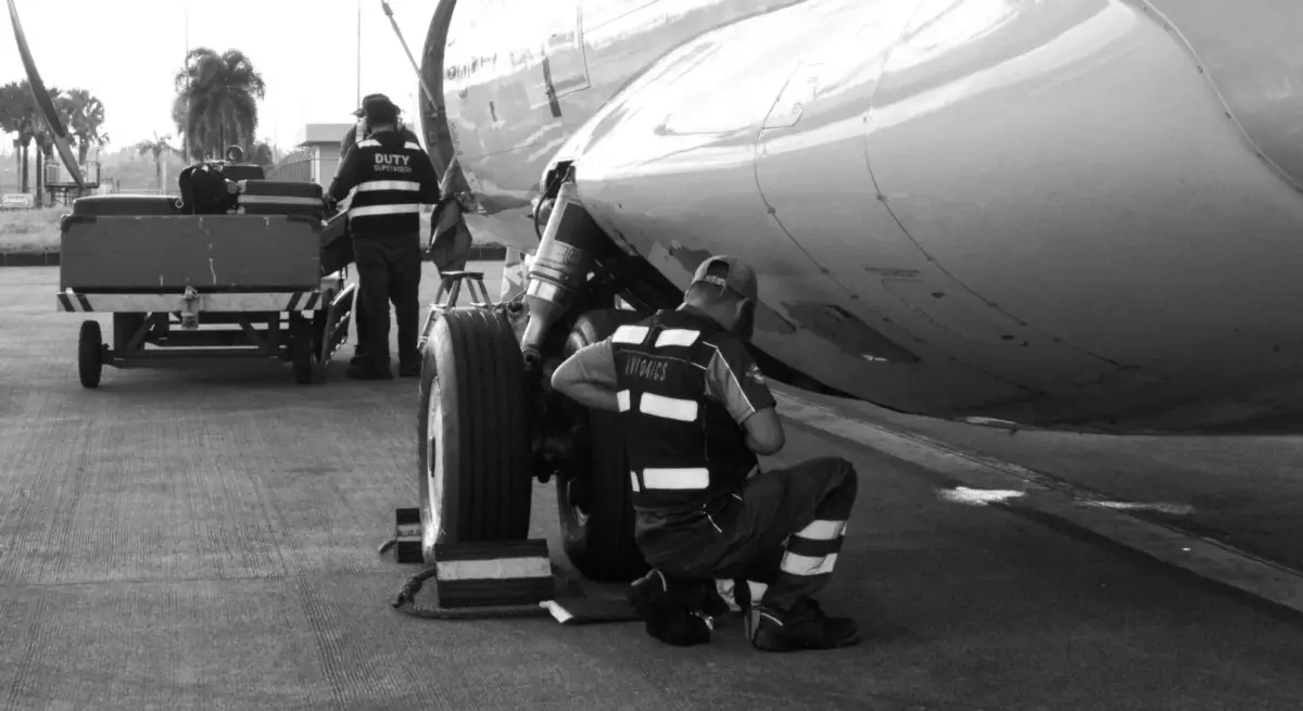 Ground crew technician inspecting private jet landing gear on tarmac while duty supervisor oversees luggage loading during pre-flight servicing