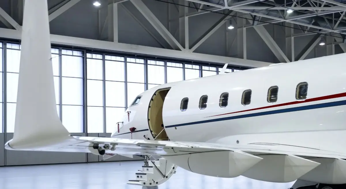 White private jet with open cabin door parked inside a modern exclusive-use hangar