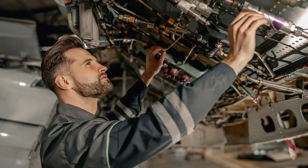 Aviation technician inspecting complex hydraulic and wiring systems beneath a private jet fuselage during a detailed safety maintenance check