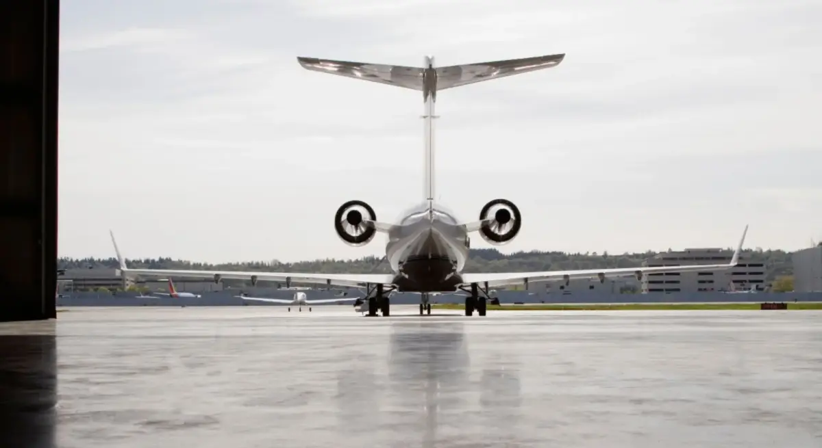 Private jet viewed from behind on airport tarmac, framed by hangar entrance, ready for international charter departure