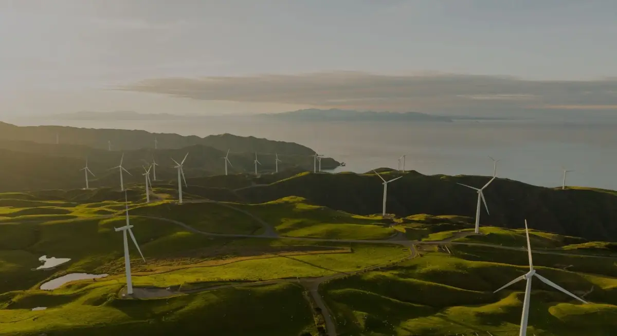 Aerial view of a coastal wind farm across green rolling hills at golden hour, representing clean energy and sustainable aviation fuel initiatives in business aviation